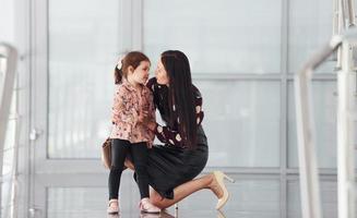 Young mother with her daughter walking together indoors in the office or airport. Having vacation photo