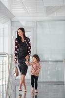 Young mother with her daughter walking together indoors in the office or airport. Having vacation photo