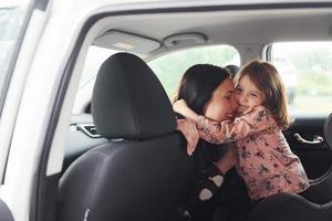 abrazándose unos a otros. madre con su hija dentro de un automóvil moderno juntos foto