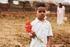 lindo niño afroamericano está en la granja en verano sosteniendo una flor roja foto