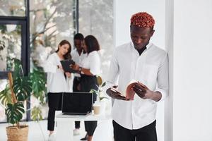 Man with notepad standing in front of colleagues. Group of african american business people working in office together photo