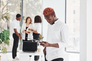 Man with notepad standing in front of colleagues. Group of african american business people working in office together photo