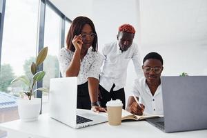 usando la misma computadora portátil para el proyecto. grupo de empresarios afroamericanos que trabajan juntos en la oficina foto