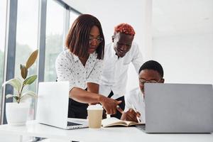 usando la misma computadora portátil para el proyecto. grupo de empresarios afroamericanos que trabajan juntos en la oficina foto