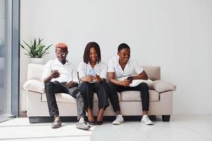 Group of african american people in formal clothes sitting on sofa indoors in office together photo