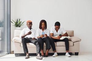 Group of african american people in formal clothes sitting on sofa indoors in office together photo