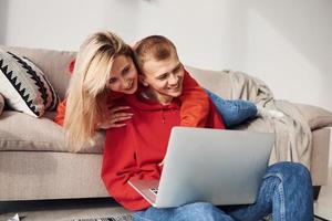Using laptop that is on the legs. Young lovely couple together at home spending weekend and holidays together photo