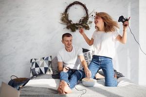 Young lovely couple together at home playing video games on bed with popcorn at weekend time photo