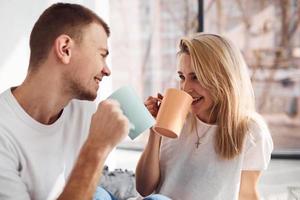 joven pareja encantadora juntos bebiendo té caliente en casa pasando el fin de semana y las vacaciones juntos