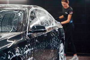 Toallitas vehiculo que esta en jabon blanco. el automóvil negro moderno es limpiado por una mujer dentro de la estación de lavado de autos foto