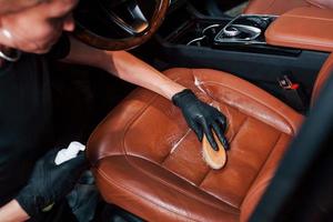 Taking care about brown colored seats. Modern black automobile get cleaned by woman inside of car wash station photo