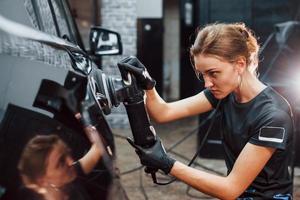 Polishing surface of vehicle. Modern black automobile get cleaned by woman inside of car wash station photo