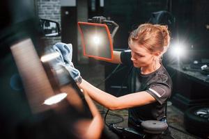 Final polishing. Modern black automobile get cleaned by woman inside of car wash station photo