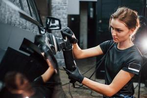 Polishing surface of vehicle. Modern black automobile get cleaned by woman inside of car wash station photo