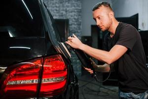 Guy polishing surface of vehicle. Modern black automobile get cleaned by man inside of car wash station photo