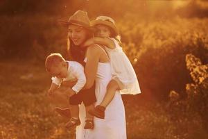 Happy family of mother, little son and daughter spending free time on the field at sunny day time of summer photo