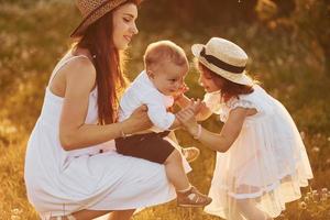 Happy family of mother, little son and daughter spending free time on the field at sunny day time of summer photo