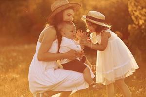 Happy family of mother, little son and daughter spending free time on the field at sunny day time of summer photo