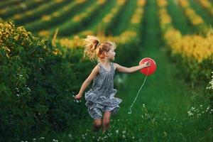 una niña positiva con un globo rojo en las manos se divierte en el campo durante el día de verano foto