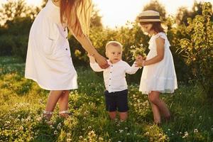 Cheerful family of mother, little son and daughter spending free time on the field at sunny day time of summer photo