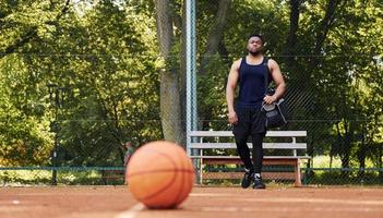 hermosos árboles verdes en el fondo. hombre afroamericano juega baloncesto en la cancha al aire libre foto