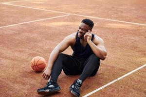 Talks by phone. African american man plays basketball on the court outdoors photo