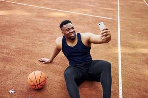 Making selfie. African american man plays basketball on the court outdoors photo