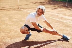 Doing warm up exercises. Senior modern stylish man outdoors on the sportive field at daytime photo