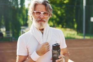 concepción de la moda. en gafas de sol. Senior hombre moderno y elegante al aire libre en el campo deportivo durante el día foto