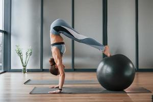 Uses fitness ball. Young woman in sportive wear and with slim body have yoga day indoors photo