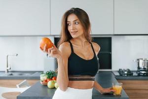 Fresh orange. Young european woman is indoors at kitchen indoors with healthy food photo