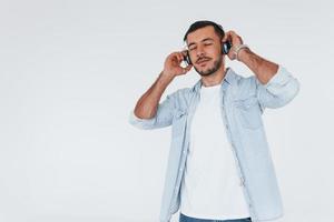 escucha la música en los auriculares. joven apuesto hombre de pie en el interior contra el fondo blanco foto