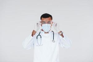 Medic in uniform. Young handsome man standing indoors against white background photo