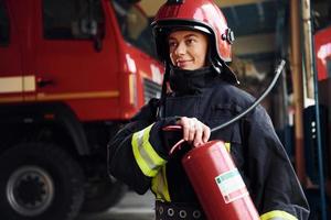 Holds extinguisher in hands. Female firefighter in protective uniform standing near truck photo