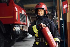 Holds extinguisher in hands. Female firefighter in protective uniform standing near truck photo