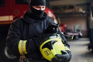 retrato de bombero con uniforme protector que sostiene un lindo gato negro foto