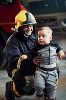 Cute little boy is with male firefighter in protective uniform photo