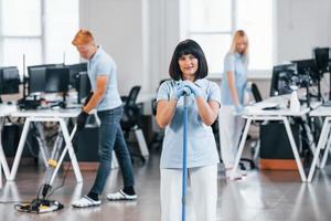 Cleans floor. Group of workers clean modern office together at daytime photo