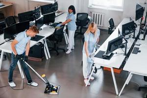 limpia piso. grupo de trabajadores limpian la oficina moderna juntos durante el día foto