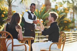 Serviced by waiter. Happy young couple is together on their vacation. Outdoors at sunny daytime photo