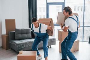 Heavy boxes. Two young movers in blue uniform working indoors in the room photo