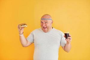 With fast food. Funny overweight man in sportive head tie is against yellow background photo