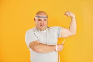 Funny overweight man in sportive head tie is against yellow background photo