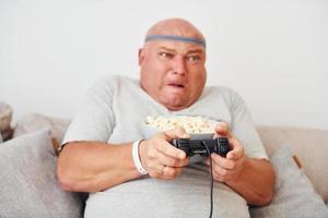Plays video game. Funny overweight man in casual clothes is indoors at home photo