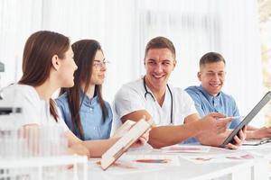 Sitting by the table. Group of young doctors is working together in the modern office photo