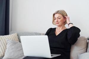 Middle-aged woman in elegant clothes is at home with laptop photo