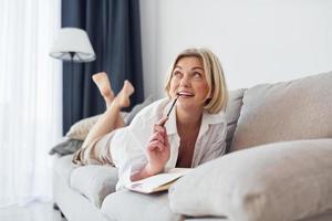 Middle-aged woman in elegant clothes is at home writing in notepad photo