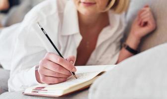 Middle-aged woman in elegant clothes is at home writing in notepad photo