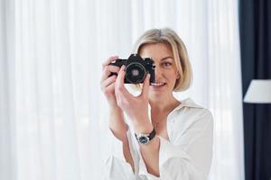 Middle-aged woman in elegant clothes is at home. Photographer with camera photo