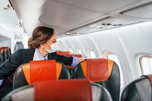 en máscara joven azafata en el trabajo en el avión de pasajeros foto